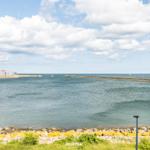 Meeresblick mit Steinhafen und Booten unter blauem Himmel.