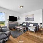 Wohnzimmer mit Sofa, Fernseher und Blick auf Balkon.