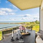Terrasse mit Tisch und Stühlen, Blick auf Meer und Strand.