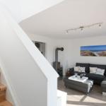 Wohnzimmer mit Sofa, Kamin und Treppe. Wandbild zeigt Strand.