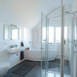 Badezimmer mit Dusche, Badewanne und Toilette. Weiße Wände und dunkle Fliesen.