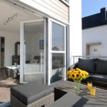 Terrasse mit Sitzgruppe und Sonnenblumen. Durchgehendes Glas führt ins Innere.