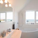 Badezimmer mit Badewanne und Meerblick durch große Fenster.