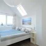 Schlafzimmer mit Blick aufs Meer, Bett, Nachttisch und Dachfenster.