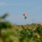 Ein Kite fliegt über eine grüne Landschaft unter blauem Himmel.