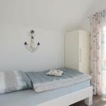 Schlafzimmer mit Bett, Garderobe und Blick auf Balkon.