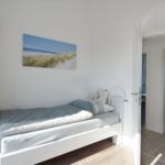 Schlafzimmer mit weißem Bett, Wandbild und Tür zum Bad.