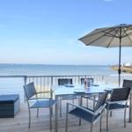 Terrasse mit Tisch, Stühlen und Sonnenschirm. Blick auf Wasser und Horizont.