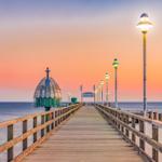 Holzsteg führt über das Meer mit beleuchteten Laternen und einer Kuppelstruktur.