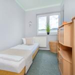 Ein Schlafzimmer mit Einzelbett, Holzschrank und Fenster mit Pflanze.