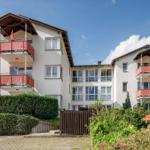 Wohnhaus mit Balkonen und grüner Umgebung unter blauem Himmel.