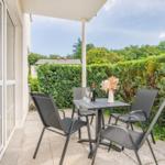Terrasse mit Tisch und Stühlen, umgeben von grünen Hecken.