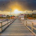 Holzbrücke führt zum Strand mit Hotels im Hintergrund.