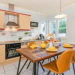 Küche mit Essbereich, Holztisch und gelben Stühlen. Fenster mit Blick auf Grün.