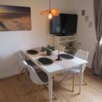 Esszimmer mit weißem Tisch, vier Stühlen und Fernseher an der Wand.