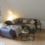 Wohnzimmer mit Ecksofa, Beistelltisch und Pflanzen auf Holzboden.