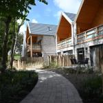 Wohnhaus mit Holzveranda und Steinmauer im Wald. Pflasterweg führt durch Grünanlagen.