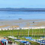 Strand mit Wattgebieten, Segelboote und Strandkörben. Menschen genießen das Wasser.