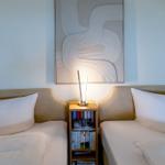 Zwei Betten mit weißen Kissen und einer Nachttischlampe zwischen ihnen.