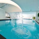 Innenpool mit Wasserfall, Metalltreppe und Pflanzen an den Wänden.