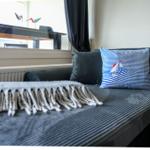 Ein Sofa mit Kissen und Decke vor einem Fenster mit Tisch und Vögeln.
