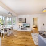 Wohn- und Essbereich mit Holzboden, TV, Sofa und Fenstern.