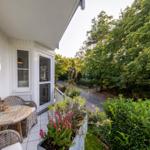 Terrasse mit Tisch, Stühlen und Pflanzen. Blick auf grüne Bäume und einen Weg.