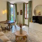 Living and dining area with TV, table, and sofa. Green curtains and windows with water view.