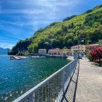 Lakeside promenade with boats and green hills in the background.