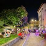 Night view of a lively street with trees, seating, and restaurants.