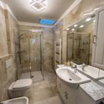 Bathroom with shower, sink, and toilet. Marble tiles and mirror cabinet.