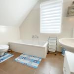 Badezimmer mit Badewanne, Waschbecken und Toilette. Fenster mit Jalousie.