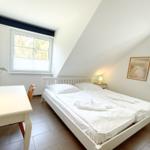 Schlafzimmer mit Doppelbett, Schreibtisch und zwei Fenstern mit Blick auf Wald.