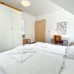 Zimmer mit Doppelbett, Schrank, Schreibtisch und Stuhl. Wandbild mit Vögeln.