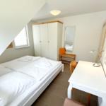 Schlafzimmer mit Doppelbett, Schrank, Spiegel und Schreibtisch.