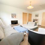 Wohnzimmer mit Sofa, Sessel und Fernseher. Tisch mit kariertem Tuch.