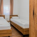 Zwei Einzelbetten mit Holzgestell und weißer Bettwäsche unter einem Fenster mit Vorhängen.