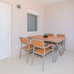 Terrassenbereich mit Tisch und vier Stühlen, weiße Tür und Fenster mit Jalousie.