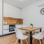 Küche mit Esstisch und Stühlen. Wanduhr und Klimaanlage sichtbar.