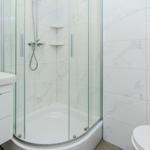 Badezimmer mit Dusche, Waschbecken und Toilette. Fliesen und Möbel sind weiß.