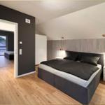 Schlafzimmer mit Doppelbett, Holzboden und Nachttischen. Durchgang zu Wohnbereich.