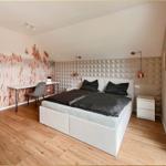 Schlafzimmer mit Doppelbett, Schreibtisch und großem Fenster. Wandtapete mit Pflanzenmotiv.