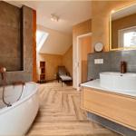 Bad mit Badewanne, Waschtisch und Dusche. Holzfußboden und warme Wandfarben.