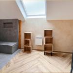 Raum mit Holzboden, Bücherregalen und Dachfenster. Wandbild und Betonbank sichtbar.