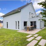 Moderne Villa mit Terrasse, Garten und Balkon. Holztisch mit Stühlen im Freien.
