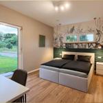 Schlafzimmer mit Bett, Schreibtisch und Fenster zur grünen Außenseite.