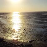 Sonnenuntergang über Wattlandschaft mit Menschen, die spazieren.