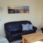 Schwarzes Ledersofa mit Kissen, Holztisch und Wandbild mit Strandmotiv.