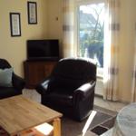 Wohnzimmer mit Sofa, Fernseher und großem Fenster mit Blick auf Garten.