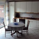 Küche mit Esstisch, Fenster zum Balkon und weißen Schränken.